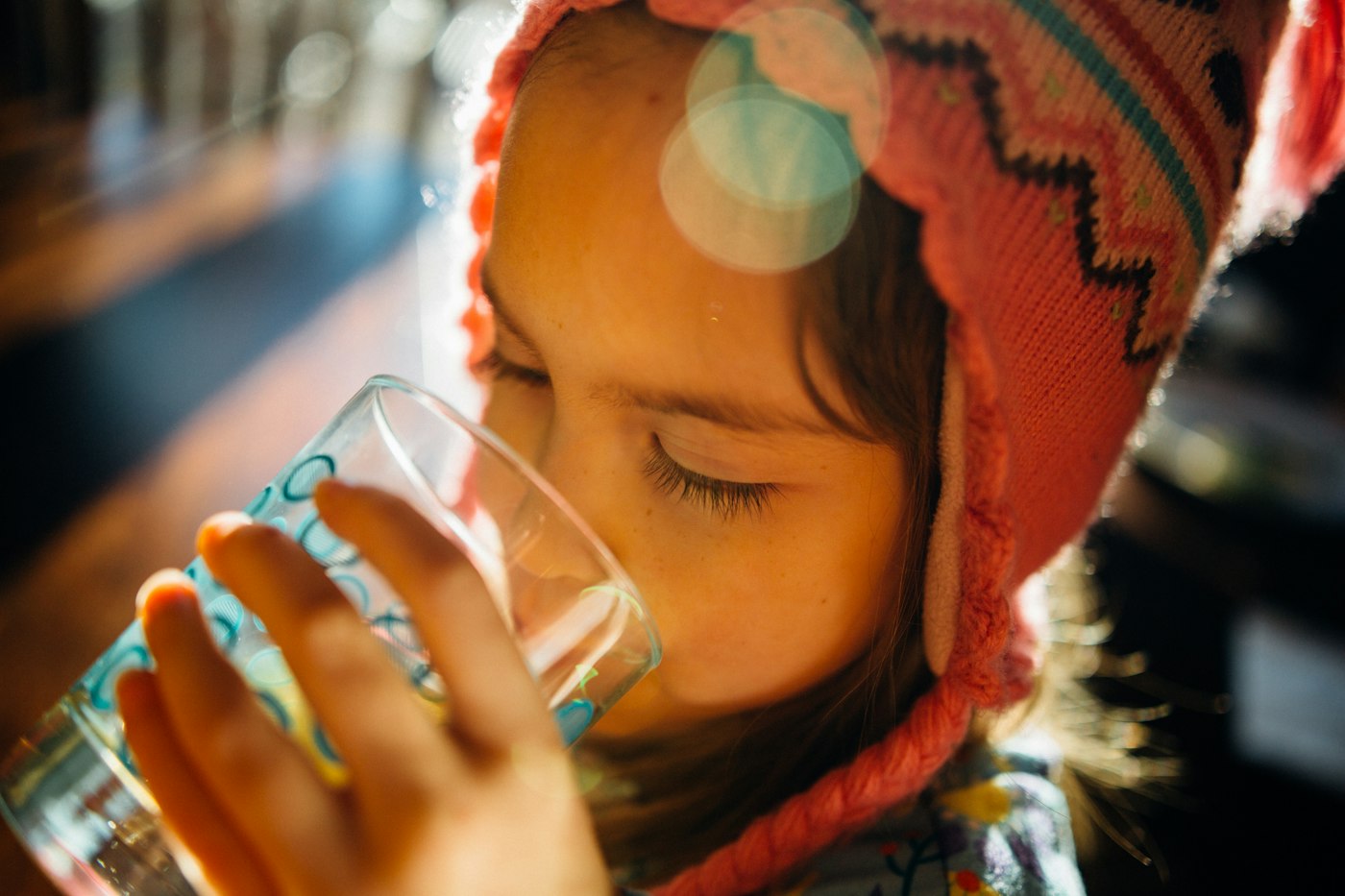 A young girl in a knit hat drinking a glass of water