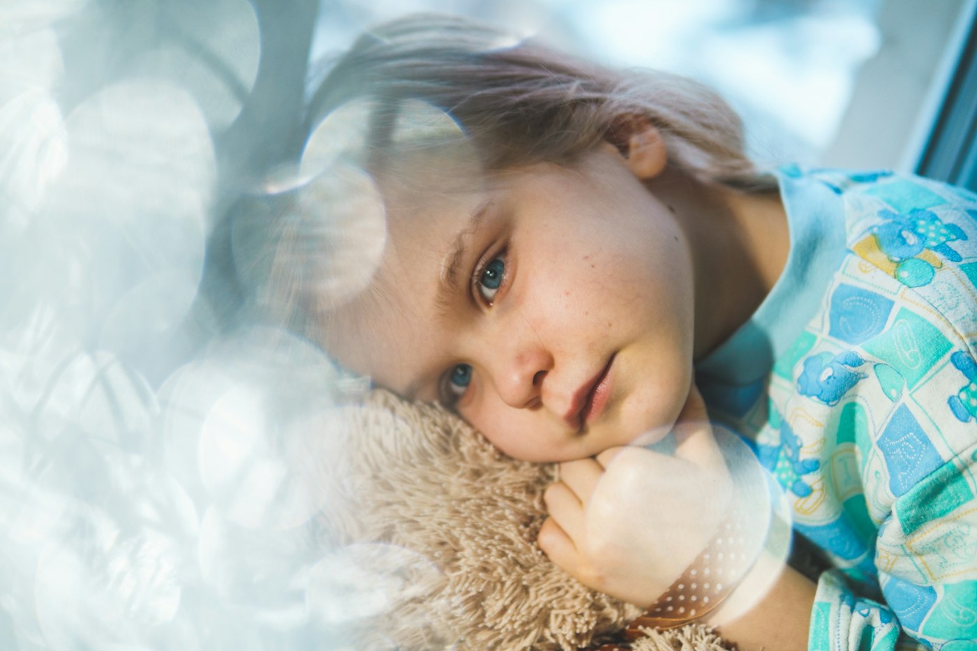 A young girl resting her head on a stuffed animal while recovering from illness