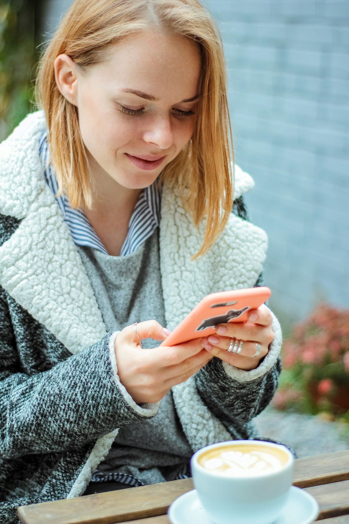A smiling woman texting on her phone at a café table