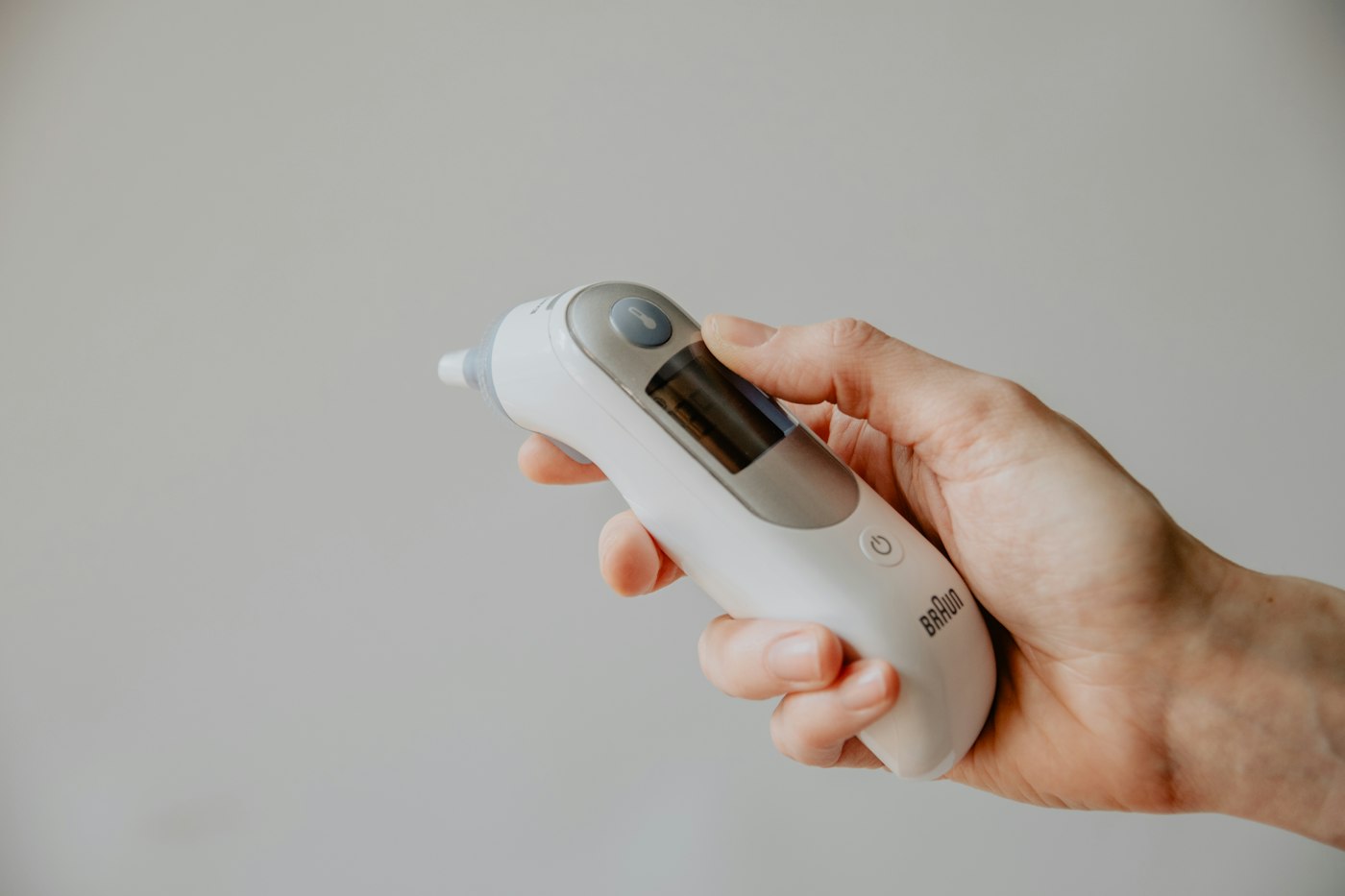 A hand holding an ear thermometer used to check a child's fever