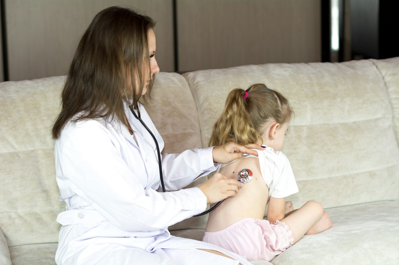 A pediatrician listening to a young girl's breathing with a stethoscope