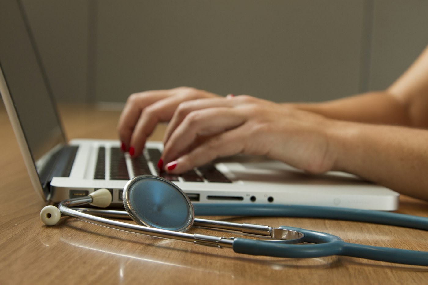 A doctor's hands typing on a laptop next to a stethoscope