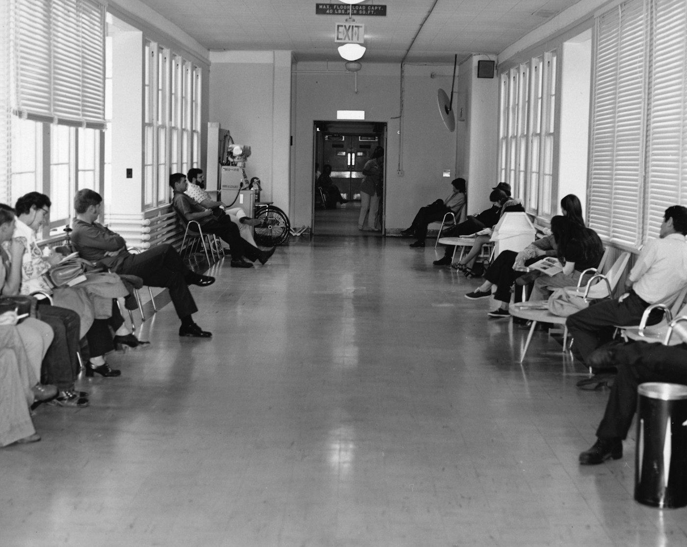 A long hospital hallway lined with people waiting in chairs